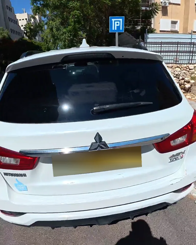 רכב מיצובישי לבן בצילום מהשטח, עם לוחית רישוי מטושטשת